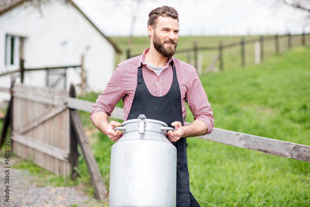 一个穿着围裙的英俊送奶工拿着牛奶容器在户外行走的肖像，回到了农村场景