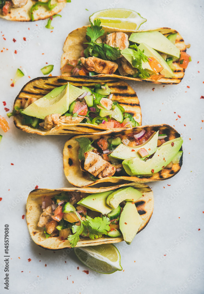 Healthy corn tortillas with grilled chicken fillet, avocado, fresh salsa, limes over light grey marb
