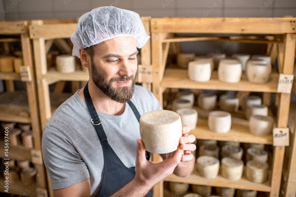 英俊的奶酪制造商站在小地窖里检查山羊奶酪的老化过程
