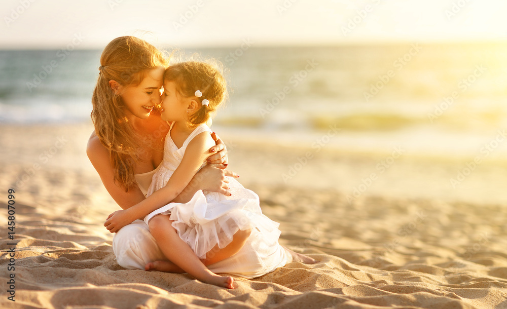 海滩上的幸福家庭。日落时母亲拥抱着小女儿