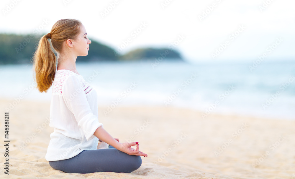 woman practices yoga and meditates in lotus position on beach.