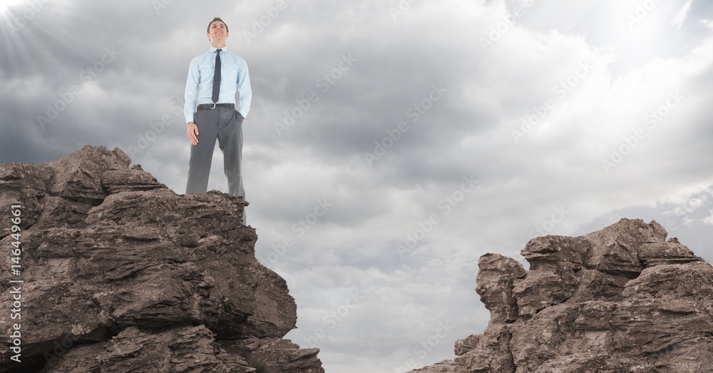 Business man hand in pocket on rocks against clouds with flare