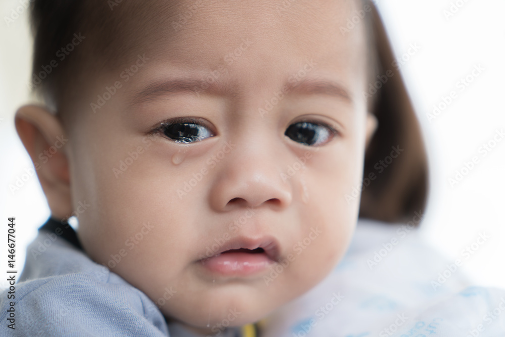 亚洲5个月大男婴在母亲怀里哭泣。
