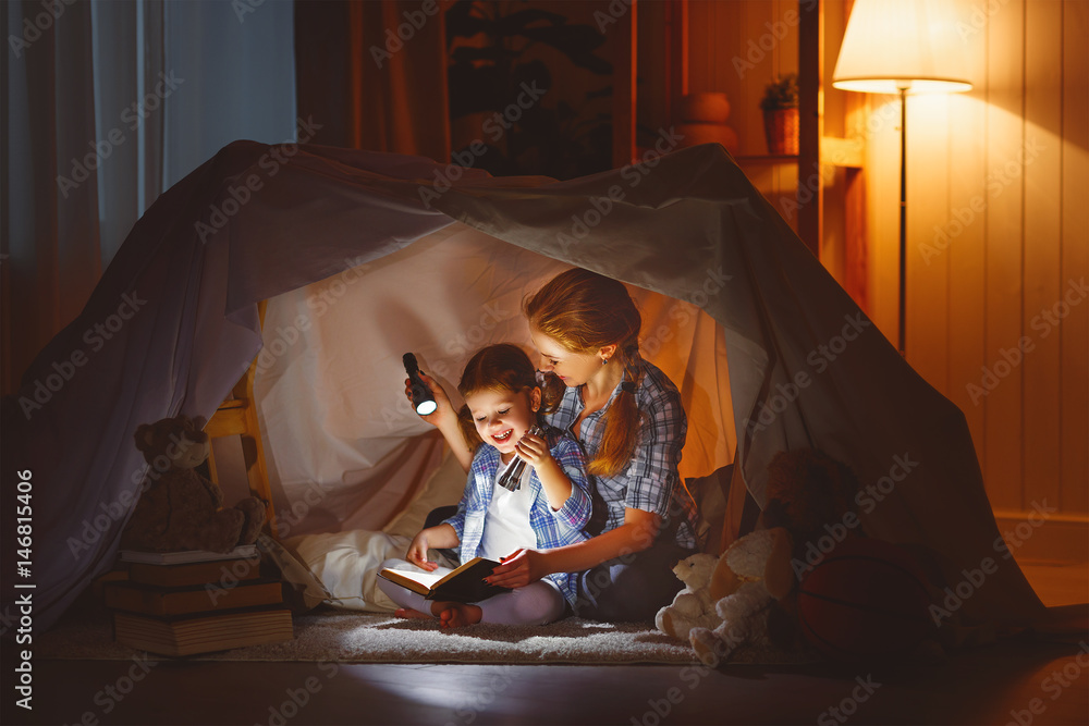 母亲和孩子女儿睡前拿着一本书和一个手电筒
