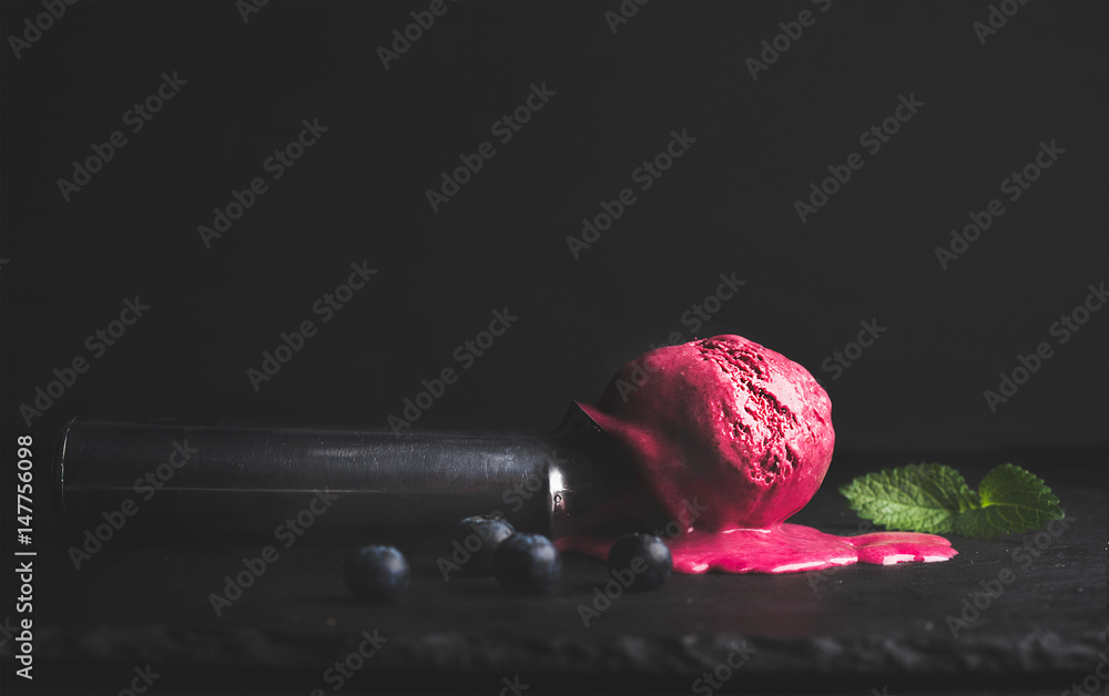 Melting blueberry ice-cream scoop over black slate stone background, selective focus, copy space, ho