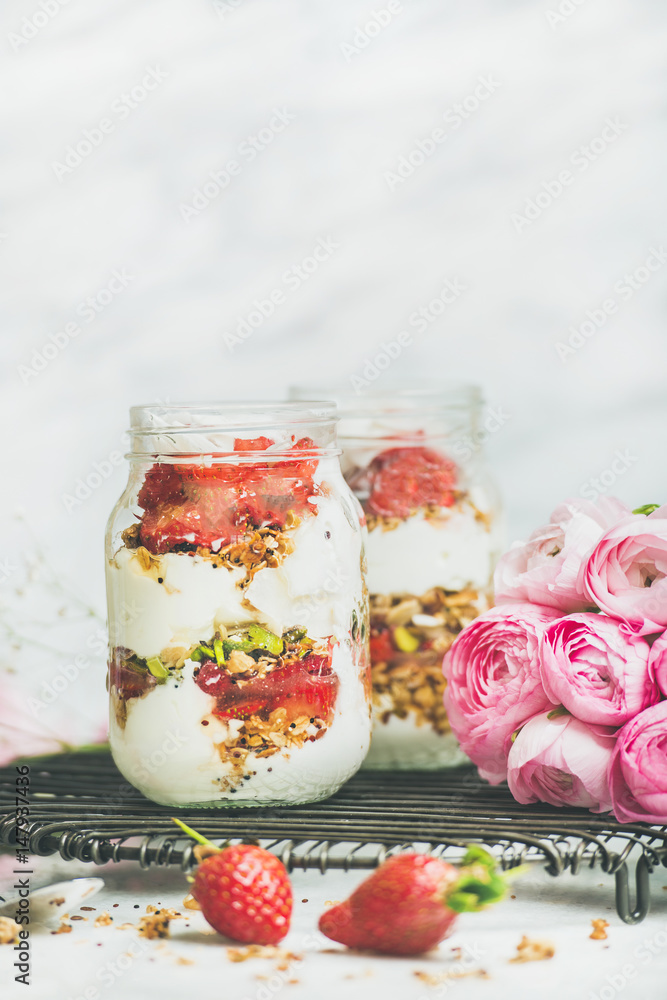 健康的春季早餐。希腊酸奶、格兰诺拉麦片、罐装新鲜草莓早餐、粉色raninkulus