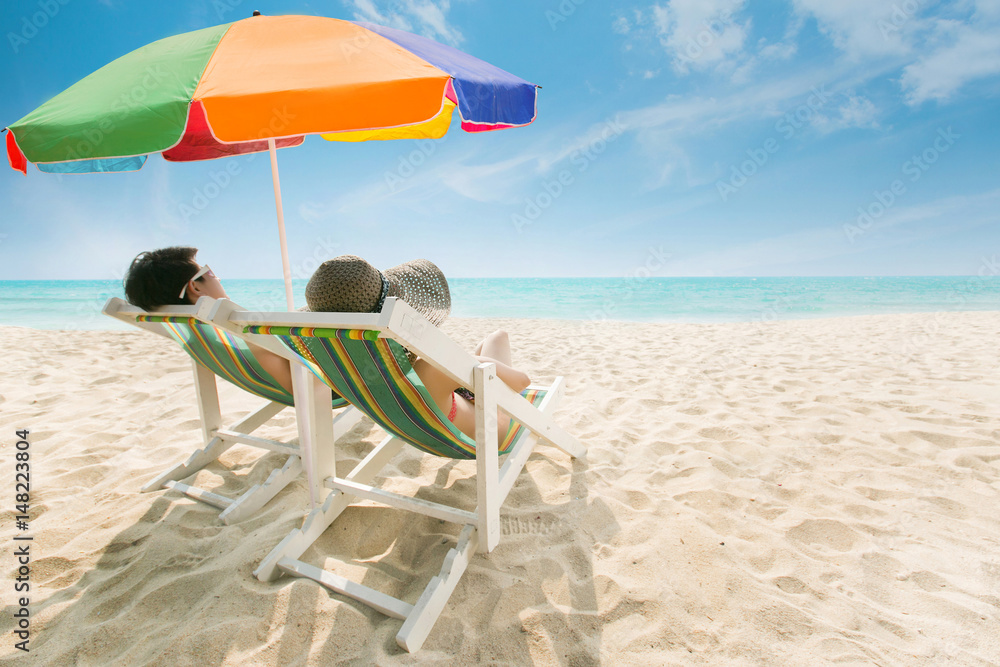 情侣在沙滩椅和雨伞上晒日光浴海滩是明亮的蓝色。夏天