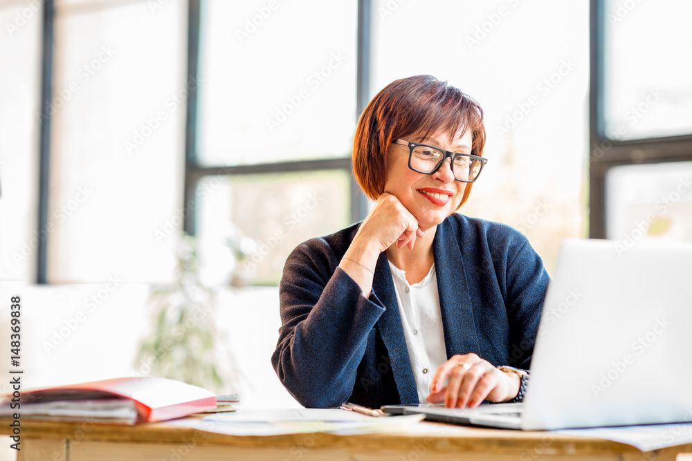 Senior businesswoman working with documents and laptop at the bright modern office interior