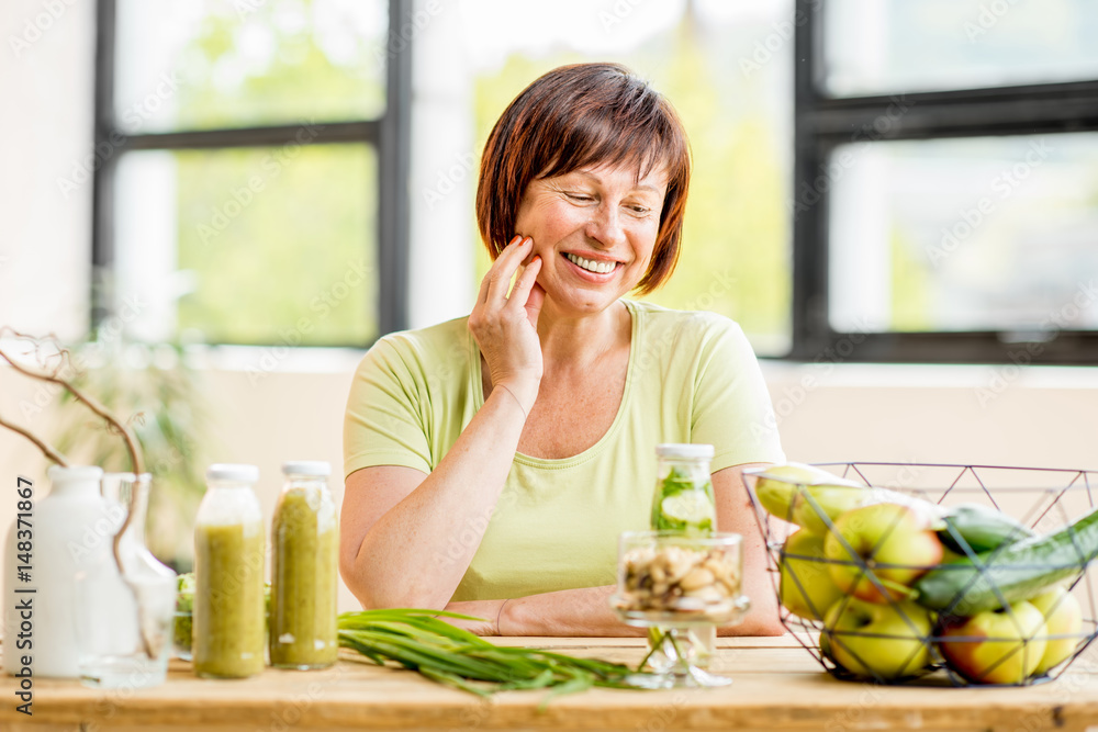一位美丽的年长女性的肖像，室内桌子上的窗户靠背上有绿色健康食品