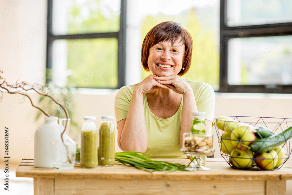 Portrait of a beautiful older woman with green healthy food on the table indoors on the window backg