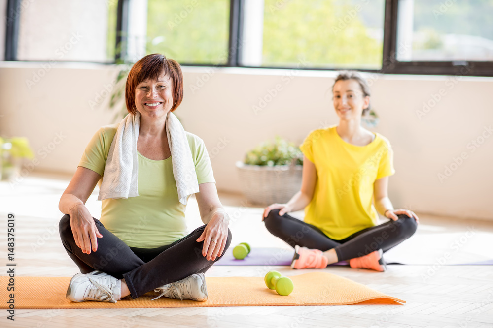 穿着运动服的年轻和年长女性在室内瑜伽训练中坐着
