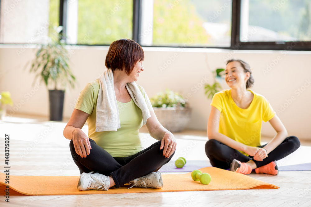 穿着运动服的年轻和年长女性在室内瑜伽训练中坐着