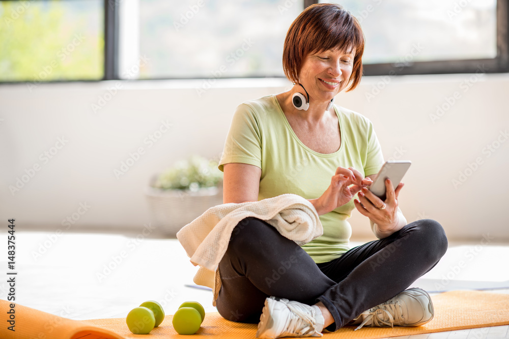 老年女性在运动训练后坐在家里或健身房的室内使用智能手机