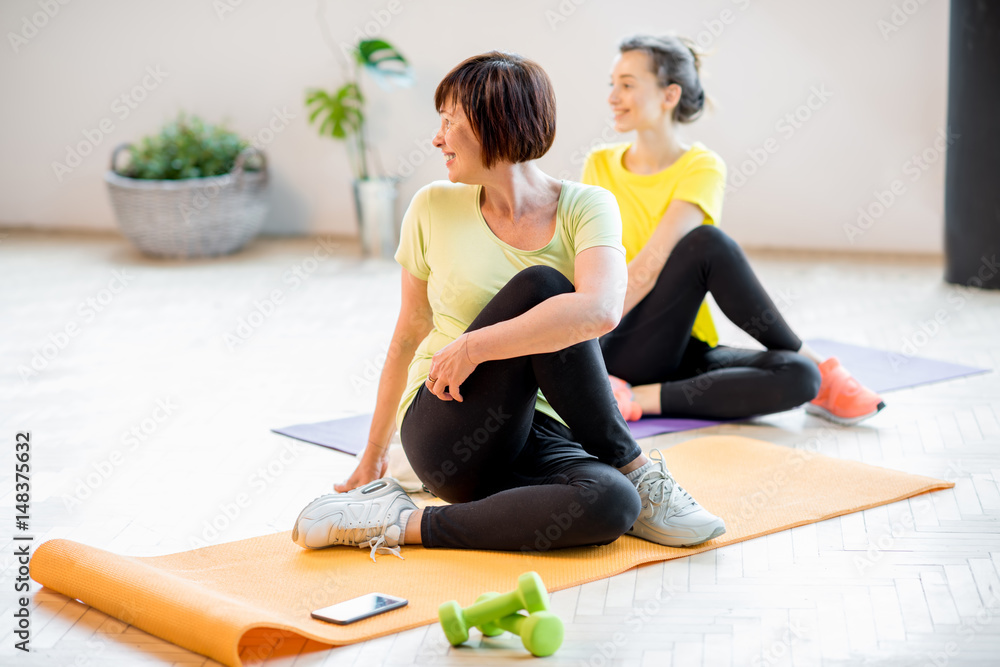 穿着运动服的年轻和老年女性在家里或健身房一起在室内做瑜伽