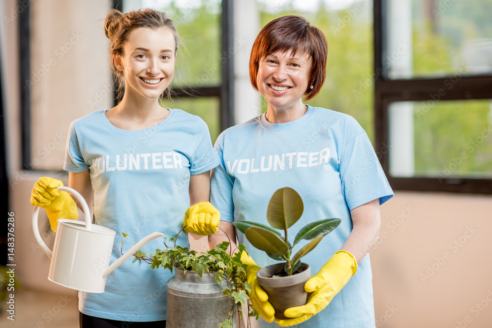 穿着蓝色t恤的年轻和年长志愿者在室内照料绿色植物
