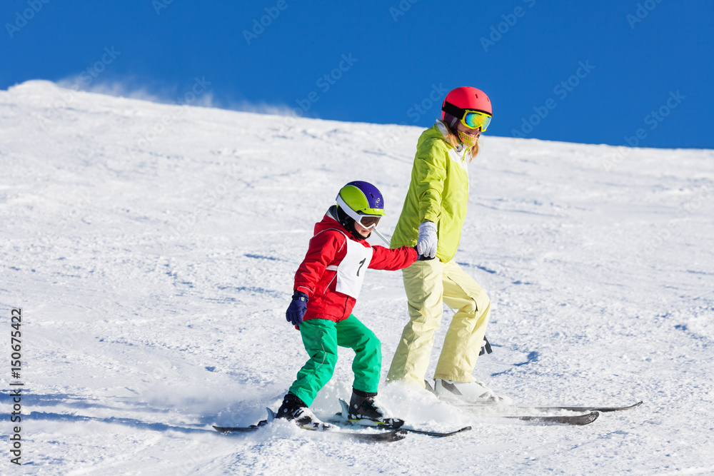 积极的母亲手牵着手教儿子滑雪