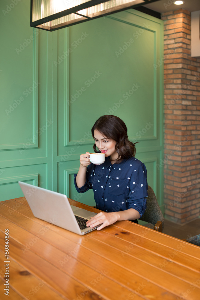 咖啡馆里漂亮可爱的亚洲年轻女商人，用笔记本电脑微笑着喝咖啡