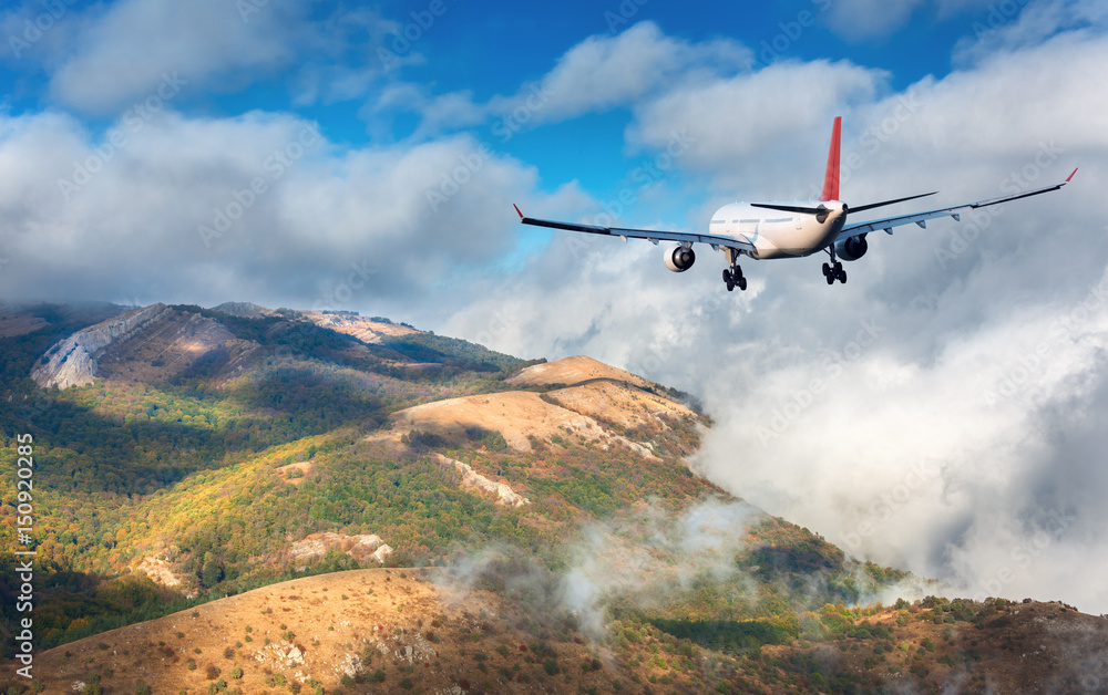 Airplane. Landscape with white passenger airplane is flying over the mountains, green forest and clo