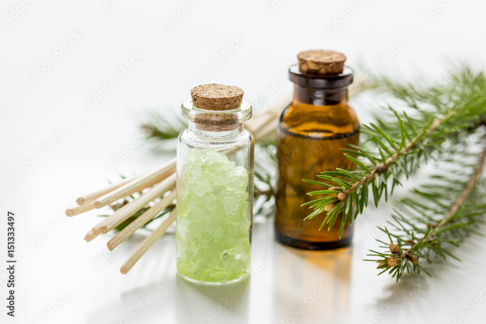 白色桌子背景上装在瓶子里的云杉针芳香疗法精油和盐