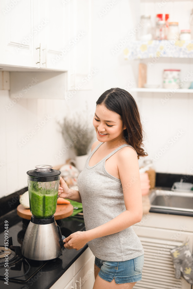 微笑的亚洲女人在家里厨房的搅拌机里用新鲜蔬菜做奶昔。