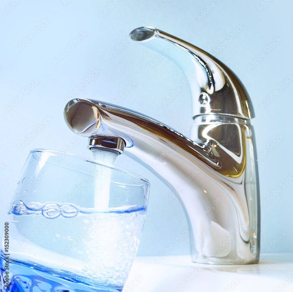 一个圆形的蓝色玻璃杯里装满了水龙头里的清水。透明的水从现代的水龙头里倒出来