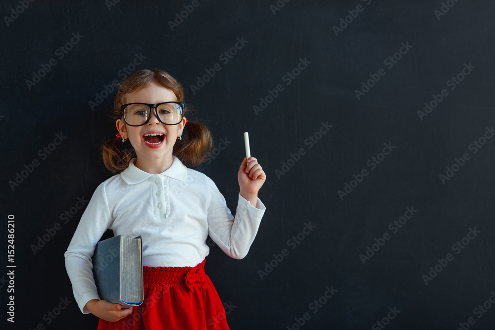 Happy schoolgirl preschool girl with book near school blackboard