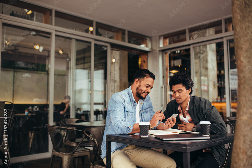 两名年轻男子坐在咖啡馆里用手机