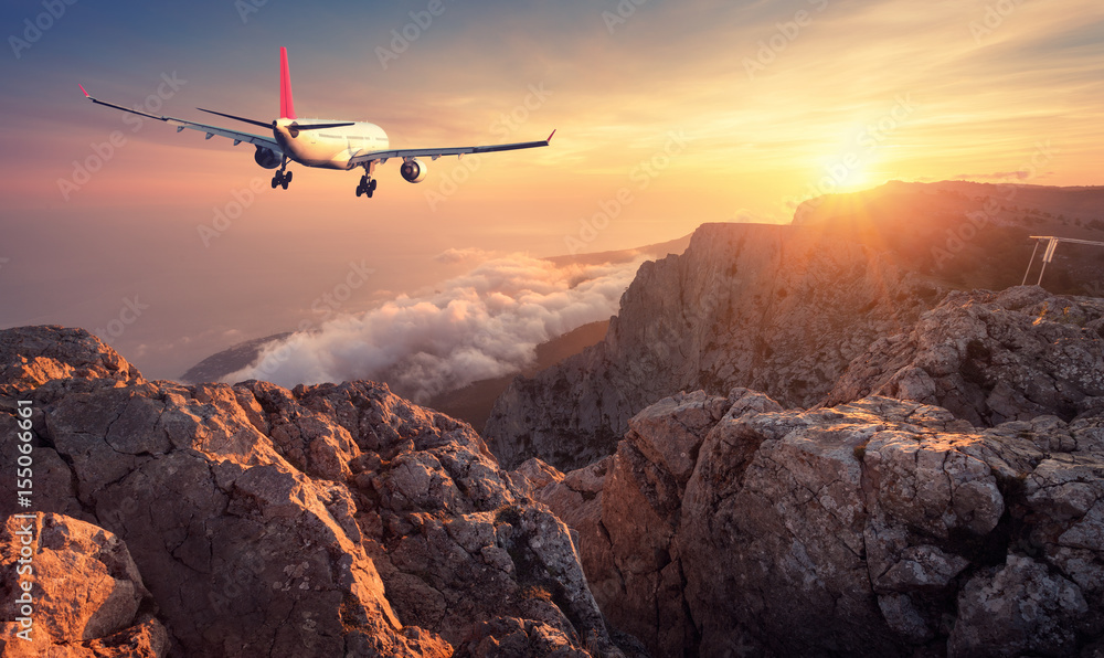 飞行的飞机。白色客机、岩石、山脉、大海和橙色天空的景观