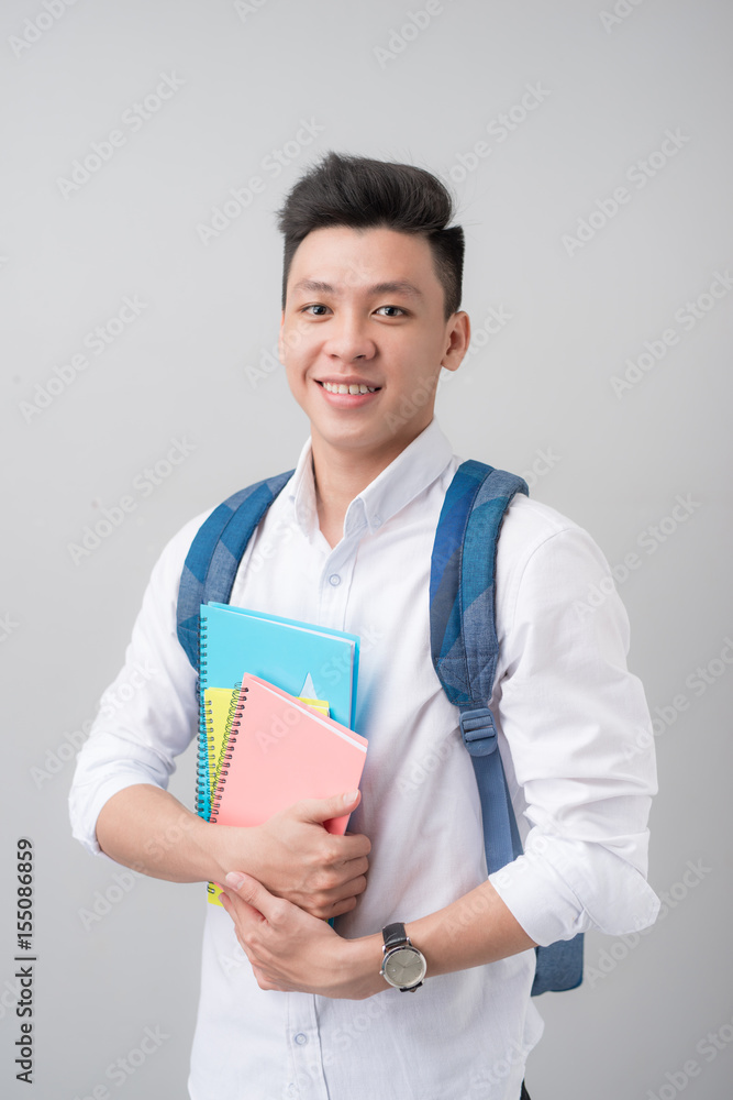 快乐随意的亚洲男学生拿着灰色背景上孤立的书