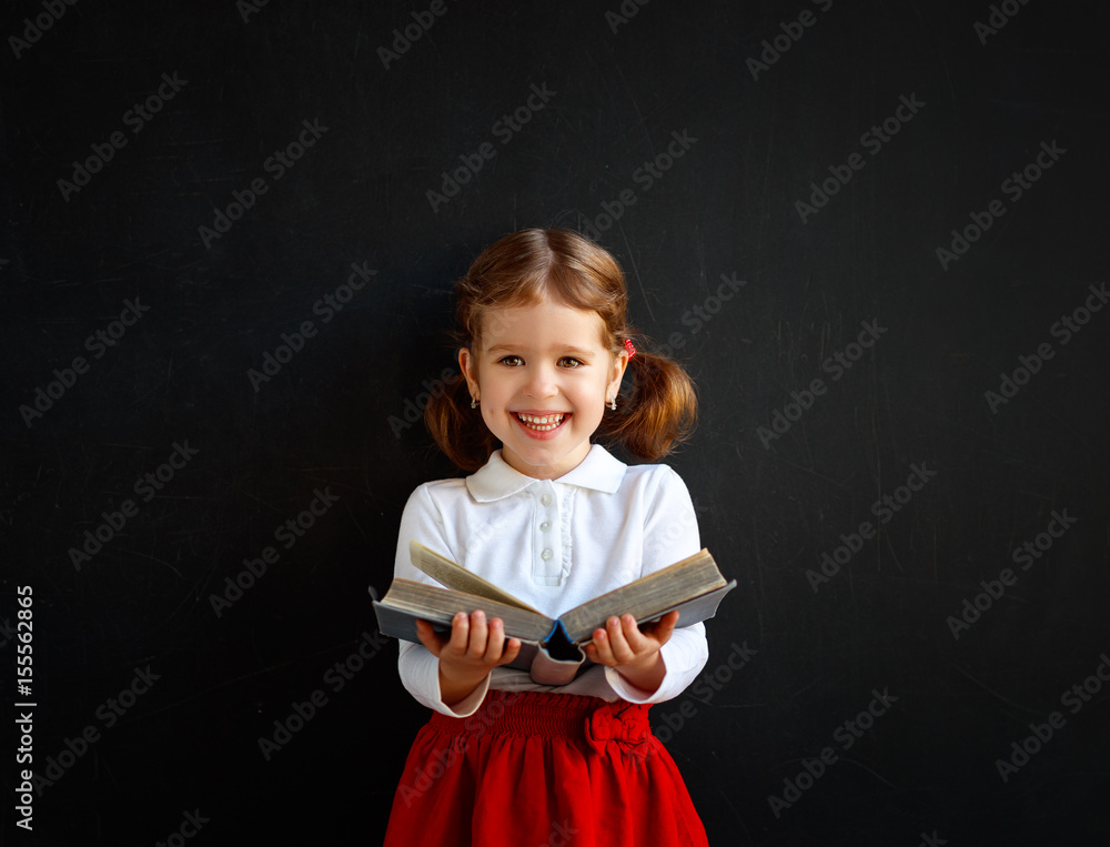快乐的学前班女孩，在学校黑板旁看书