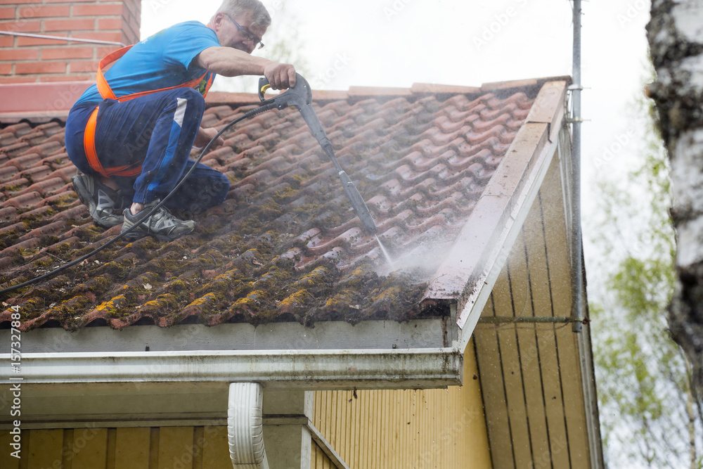 一名白人男子正在用高压洗衣机清洗屋顶。他在一辆sli上戴着安全带