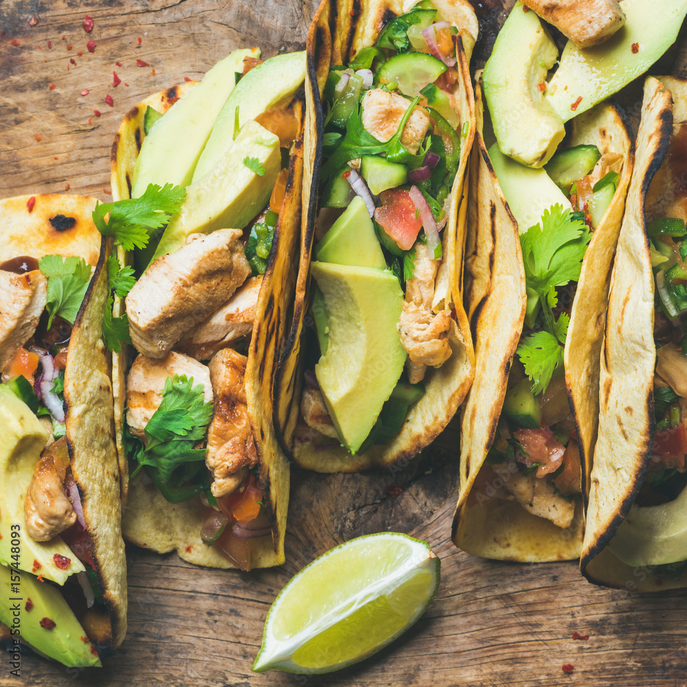 Tacos with grilled chicken, avocado, fresh salsa and limes over rustic wooden background, top view, 