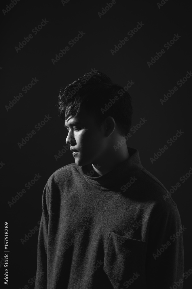 Attractive asian man looking down to his side on dark studio background.