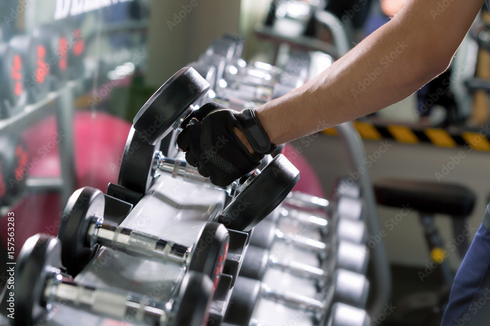 在现代健身房里，一名运动男子在做一排排金属的单臂哑铃。
