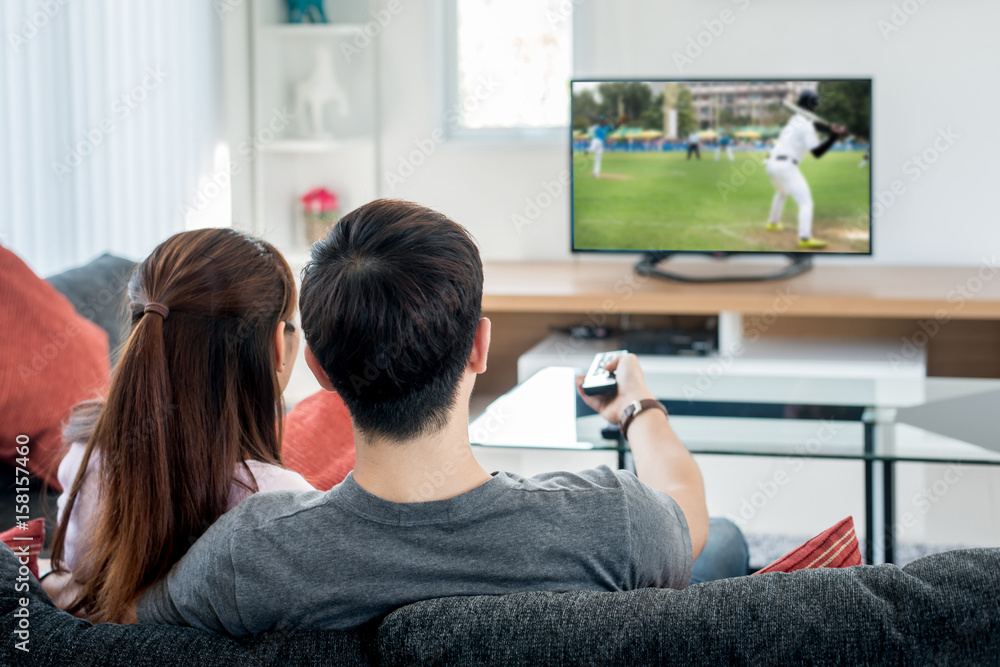 年轻的亚洲夫妇在家里的电视上漫步棒球运动