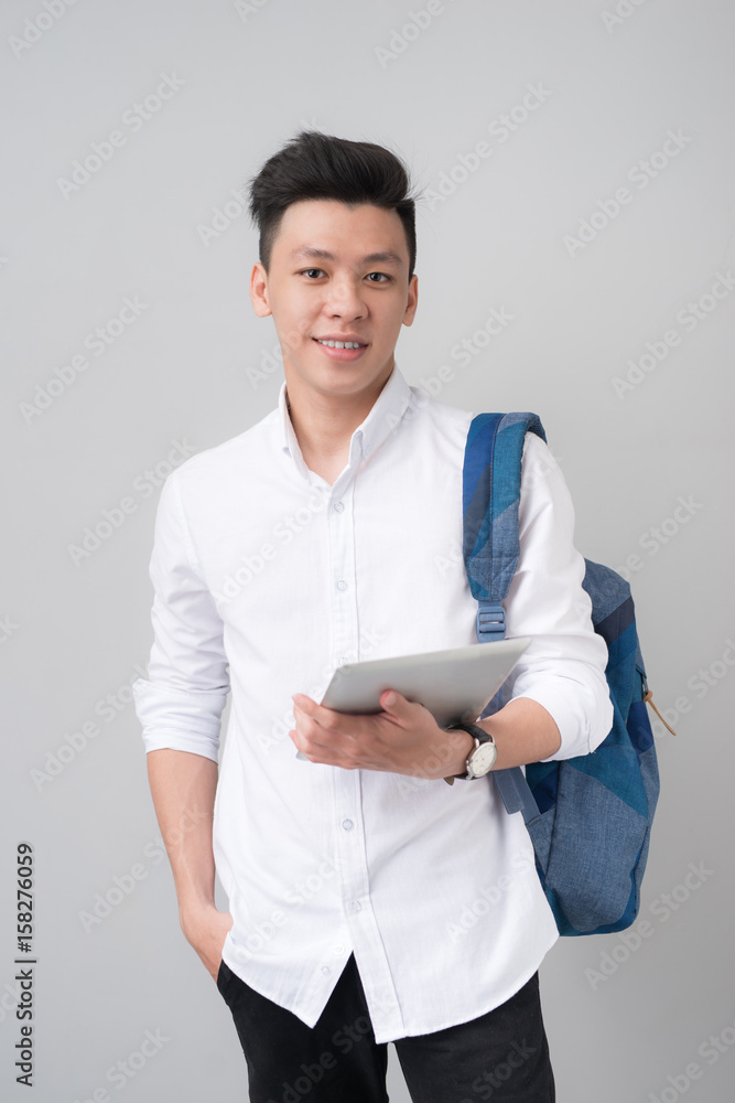 快乐的休闲亚洲男学生使用灰色背景下隔离的平板电脑