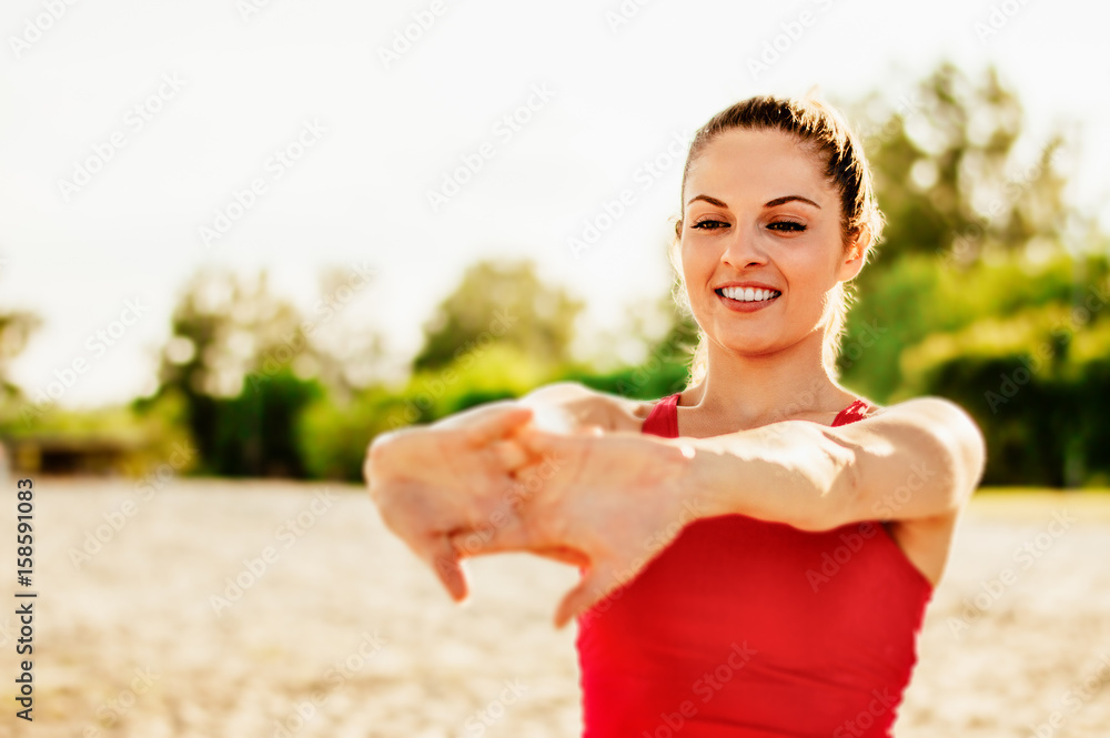 年轻女子在户外伸展手臂。健身女性在海滩上做热身运动。