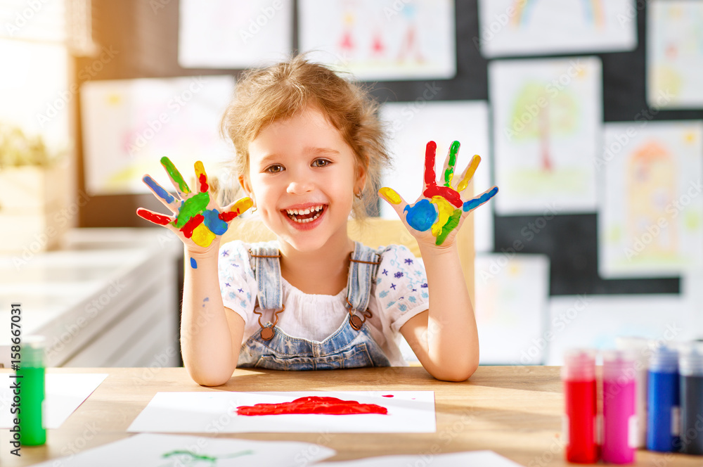 有趣的小女孩画画大笑，手被油漆弄脏
