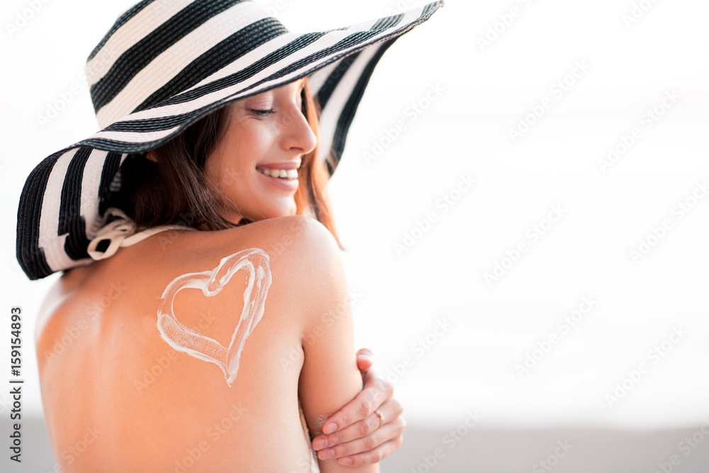 戴条纹帽子，肩上有防晒心形的美女在海滩上晒日光浴