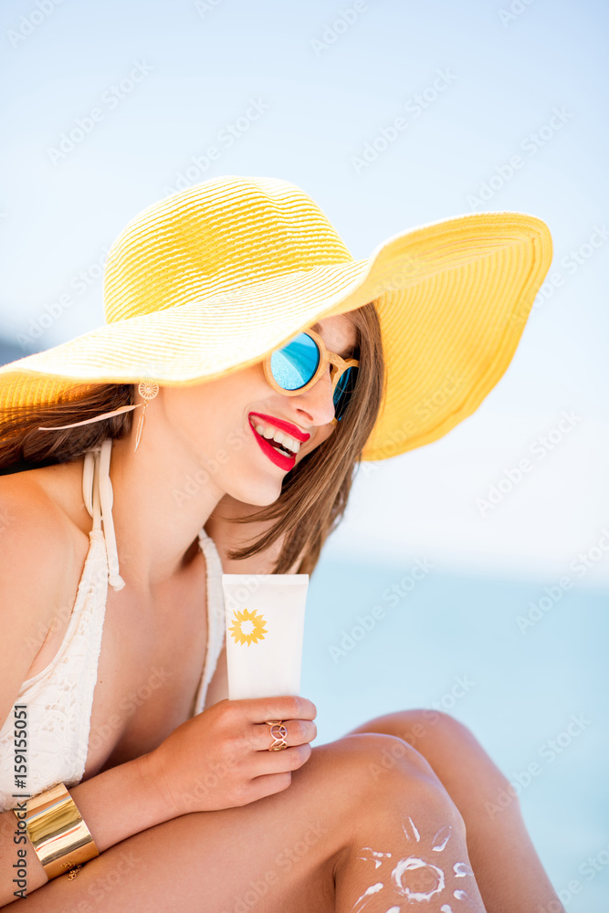 戴着黄色帽子的美丽微笑的女人拿着一瓶防晒紫外线防护乳液进行日光浴