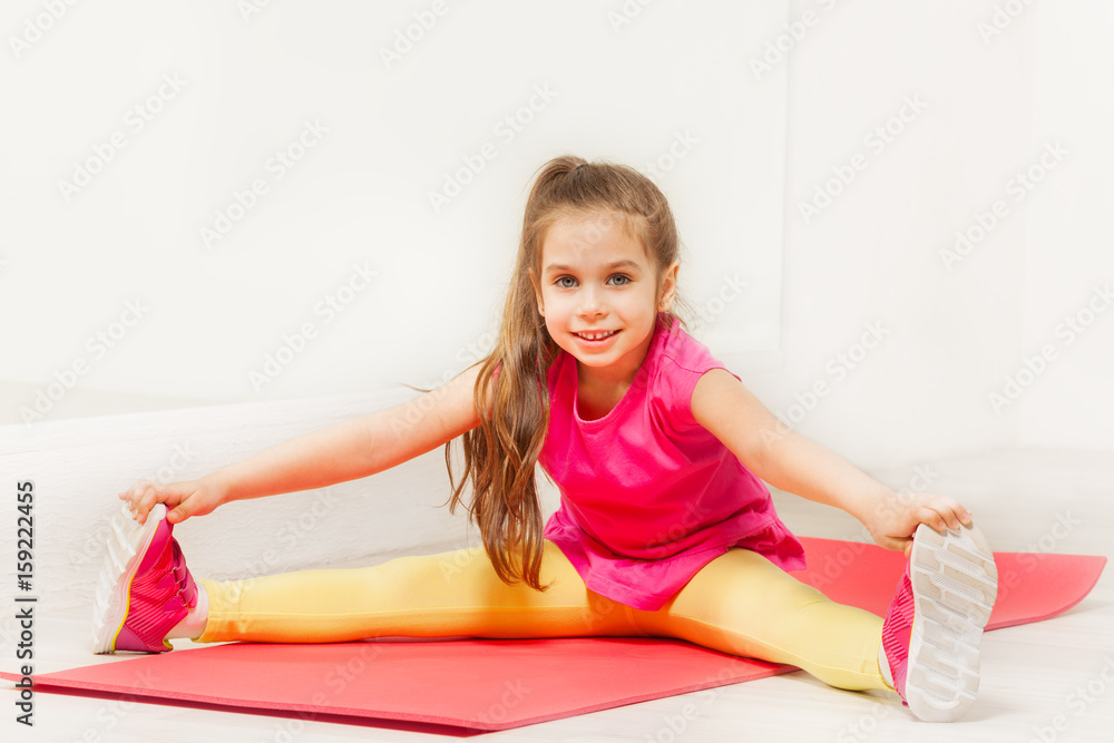 Little gymnast stretching legs on yoga mat