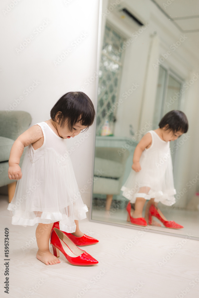 可爱有趣的小女婴在家里试着妈妈穿红色高跟鞋