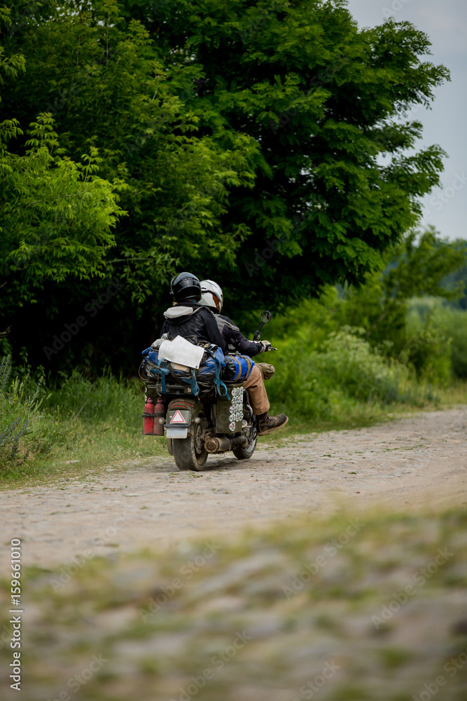 Man riding motorcycle with a woman on rural road. Young couple on motorbike through country road. Co