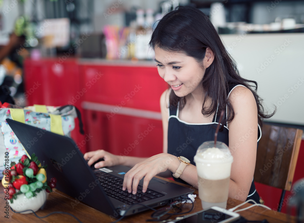 亚洲女人用电脑工作，喝冰咖啡