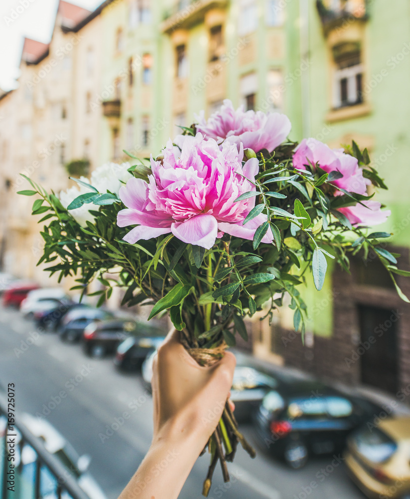 女人手里拿着粉红色和白色的牡丹花，街道背景。鲜花贺卡骗局