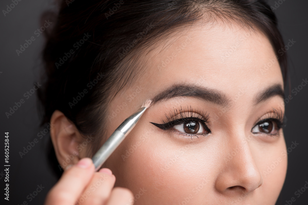 正在化妆的年轻亚洲女性美丽面孔特写。艺术家正在涂抹眼影