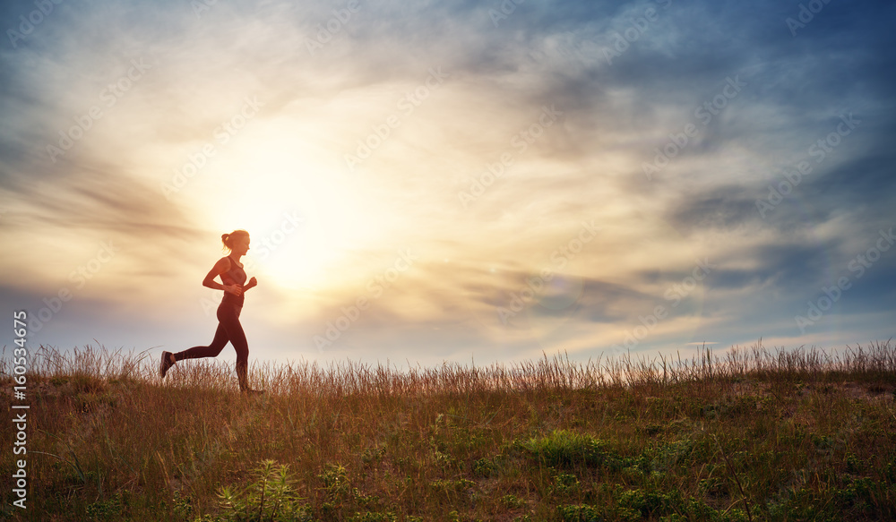 日落时分，一名年轻女子在海边的田野上奔跑。黄昏时分，活跃在户外的人在summe