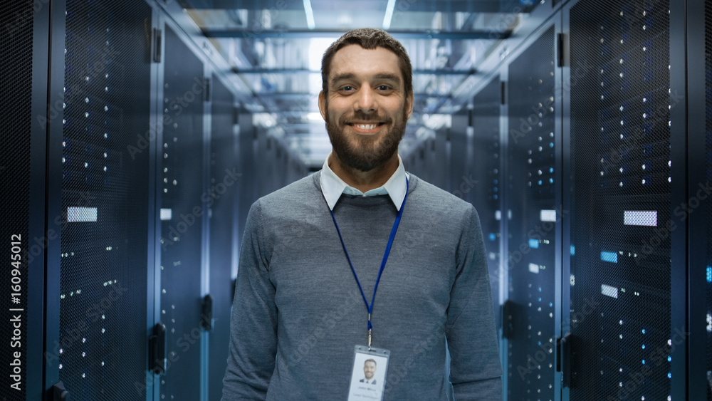 站在大型数据中心中央的古玩、积极和微笑的IT工程师肖像