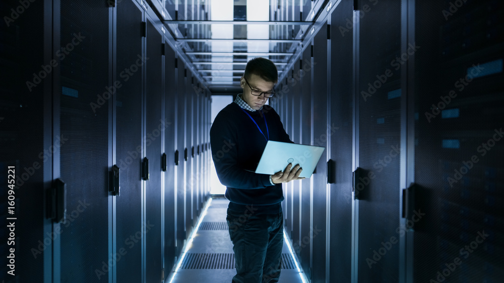 男IT工程师在大数据中心服务器机柜前的笔记本电脑上工作。一排排机架系列