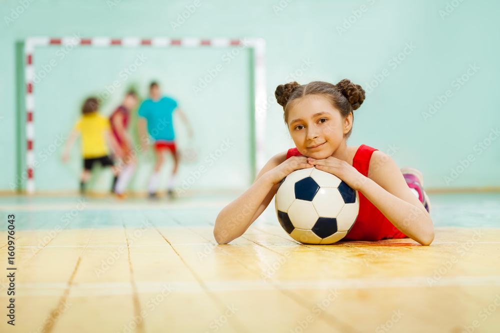 女孩拿着球躺在体育馆地板上